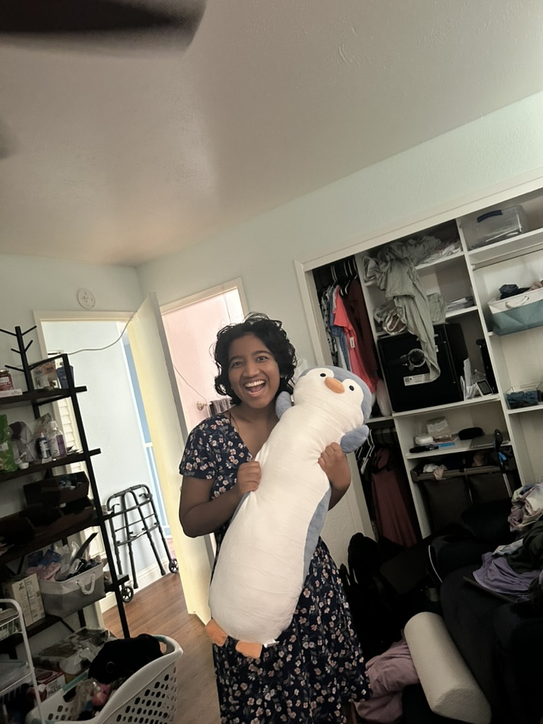 Harshini holding a plush penguin toy close, smiling with visible joy indoors.