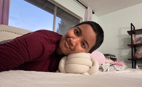 Harshini lying on a bed, resting her head on a sensory plush toy and smiling gently.